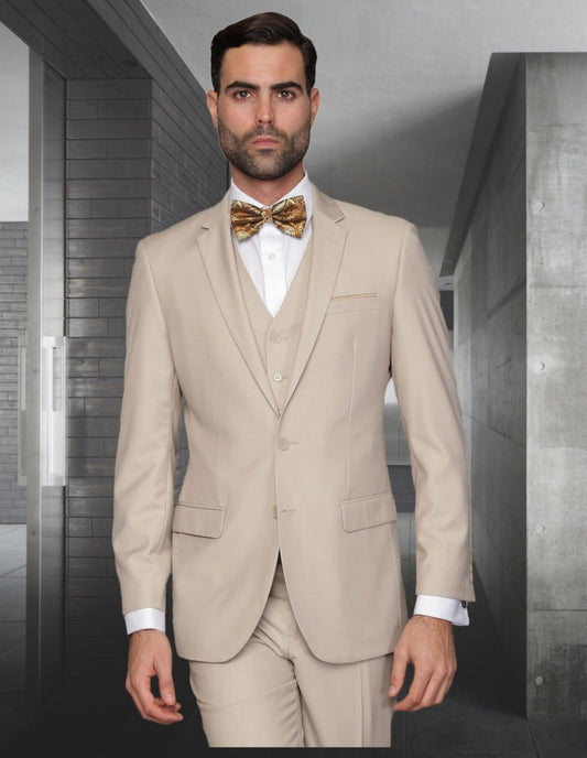 A man in a slim fit, Lorenzo-tan suit by Statement Clothing with flat front pants and a gold bow tie stands in a modern hallway.