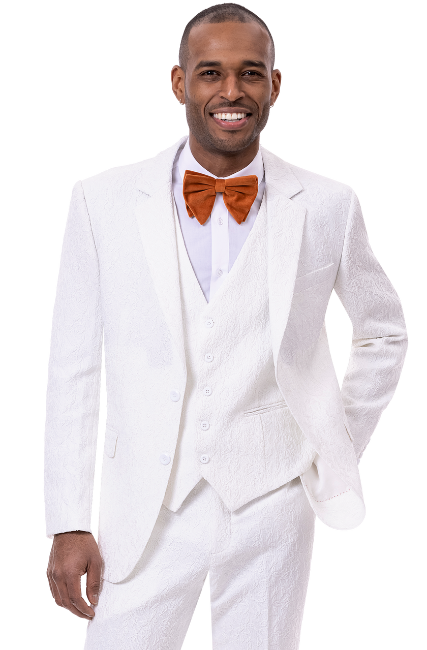 A man in an EJ Samuel White Suit M2763, featuring a stylish textured design, confidently smiles while wearing an orange bow tie and stands with one hand in his pocket.