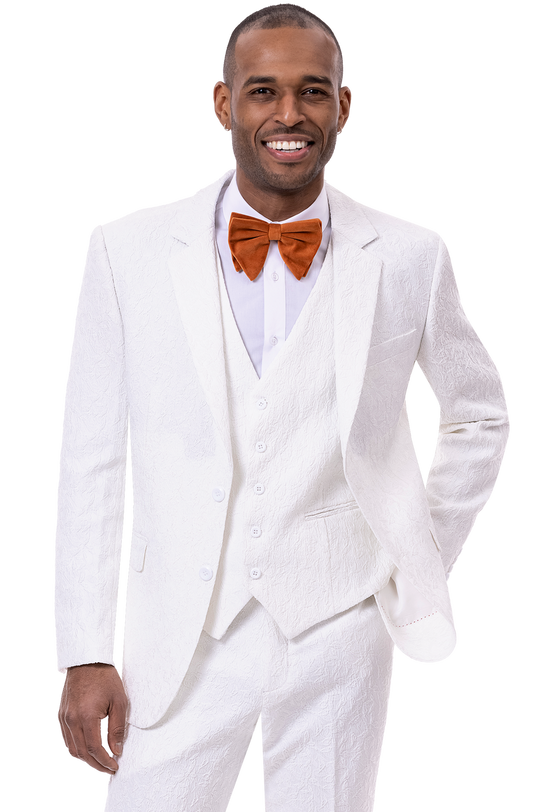 A man in an EJ Samuel White Suit M2763, featuring a stylish textured design, confidently smiles while wearing an orange bow tie and stands with one hand in his pocket.