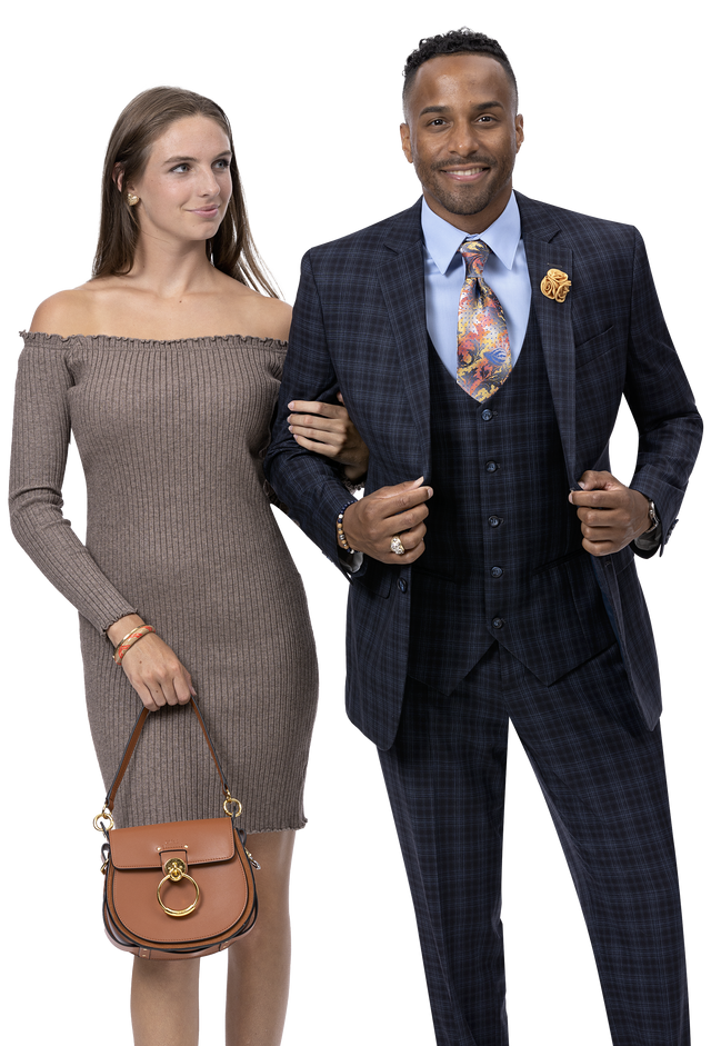 A woman in a stylish off-the-shoulder dress stands arm in arm with a man wearing the EJ Samuel Black Suit M2778, highlighting their impeccable fashion sense. She elegantly holds a brown handbag.