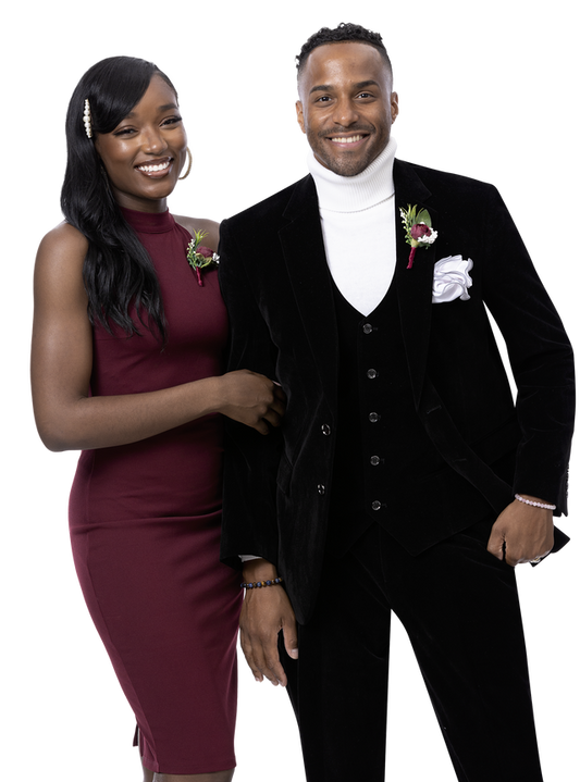 A smiling couple dressed in formal attire showcases fancy fashion, with the woman in a burgundy dress and the man wearing the EJ Samuel Black Suit M2781 paired with a white turtleneck, both adorned with floral boutonnieres.