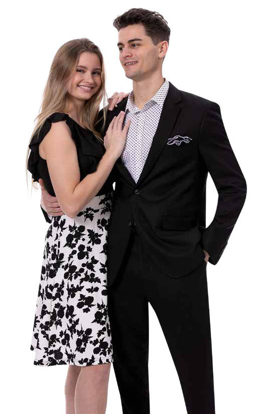 A smiling couple poses together, with the woman wearing a black and white floral dress made from a soft linen blend fabric, while the man complements her in the stylish EJ Samuel Black Suit M2792 from EJ SAMUEL, paired with a polka dot shirt.