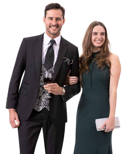 A man wearing the EJ SAMUEL Black Suit M2795 holds a wine glass while standing next to a woman in a dark green dress, holding a clutch. They smile and pose against a white background.