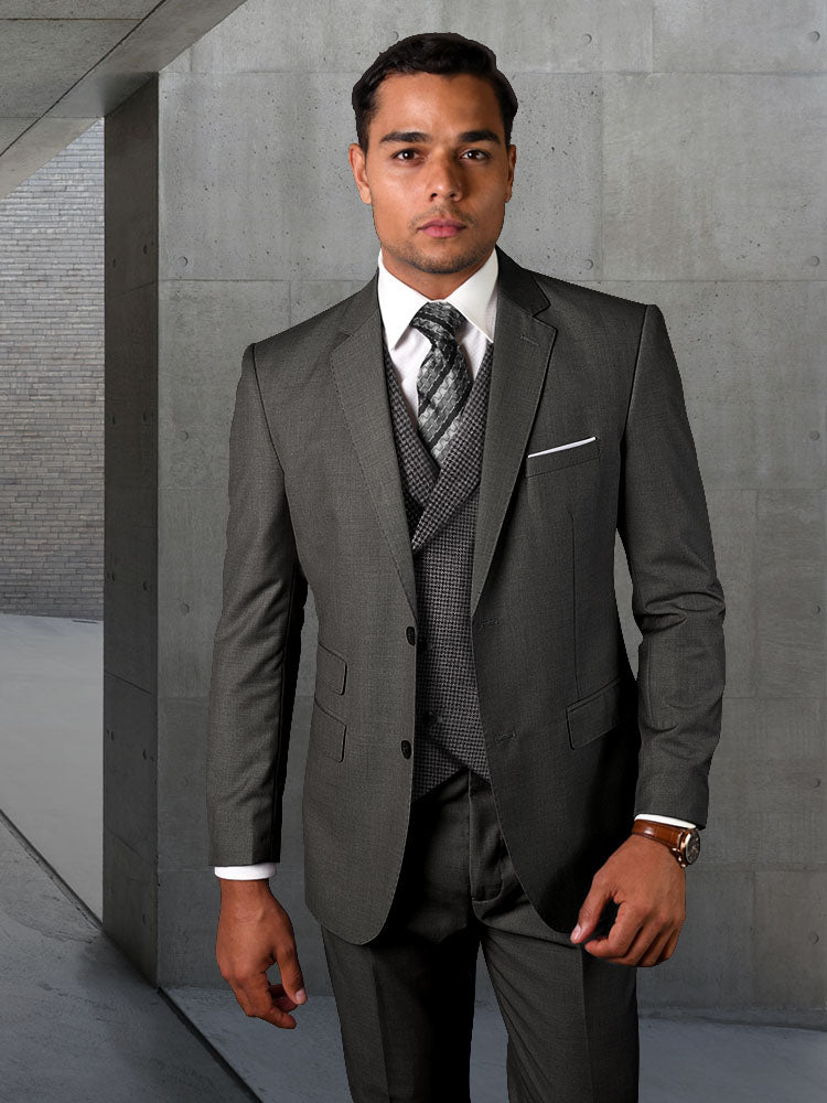 A man wearing the STATEMENT CLOTHING | MARCO-CHARCOAL from Statement Clothing, featuring modern fit pants and a tie, stands in a sleek concrete hallway, facing forward.