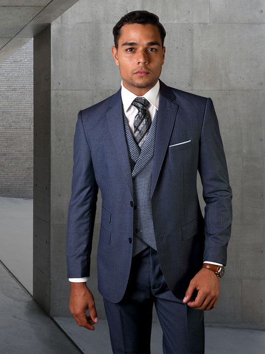 A man in the STATEMENT CLOTHING | MARCO-INDIGO suit crafted from luxurious Italian wool, complemented by a patterned tie, stands confidently against a concrete wall, looking directly at the camera.