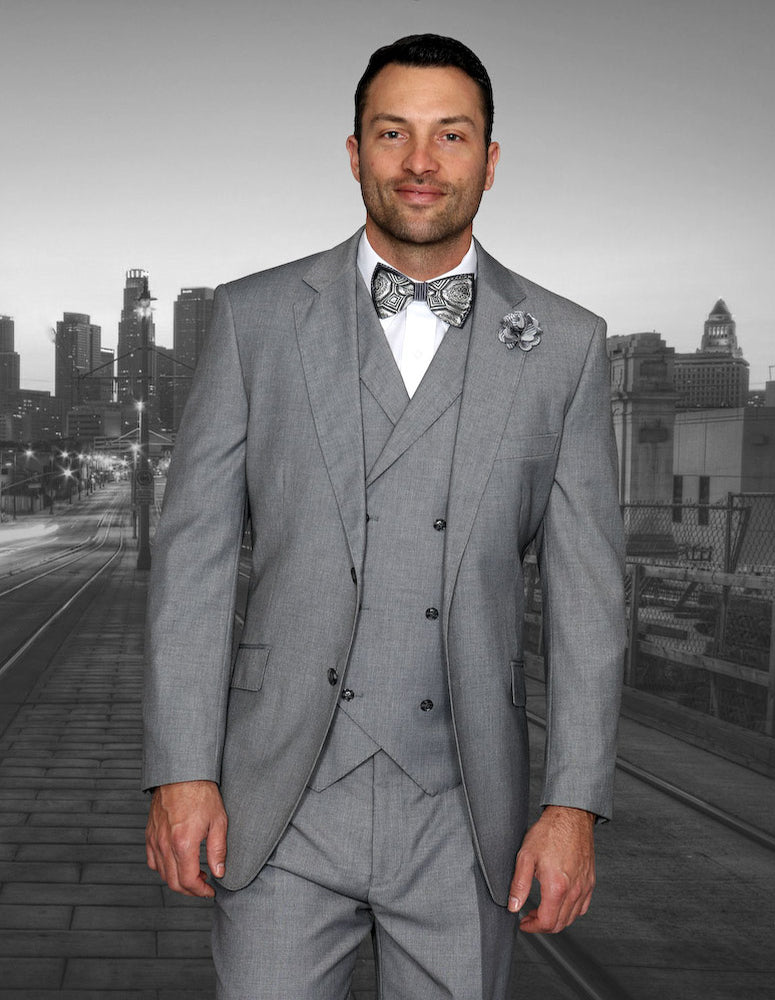 Dressed in the MESSINA-GREY three-piece suit by Statement Clothing, a man with a distinguished look stands against a cityscape background; his ensemble includes a double-breasted vest and pleated pants.