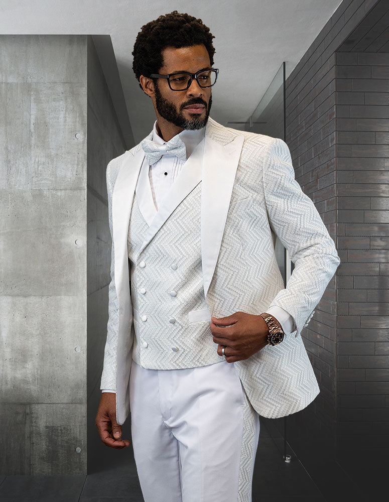 A man in the Statement Clothing MIRAGE-WHITE tuxedo, featuring a patterned style and peak lapel, along with a bow tie, stands in a modern room with concrete and tiled walls.