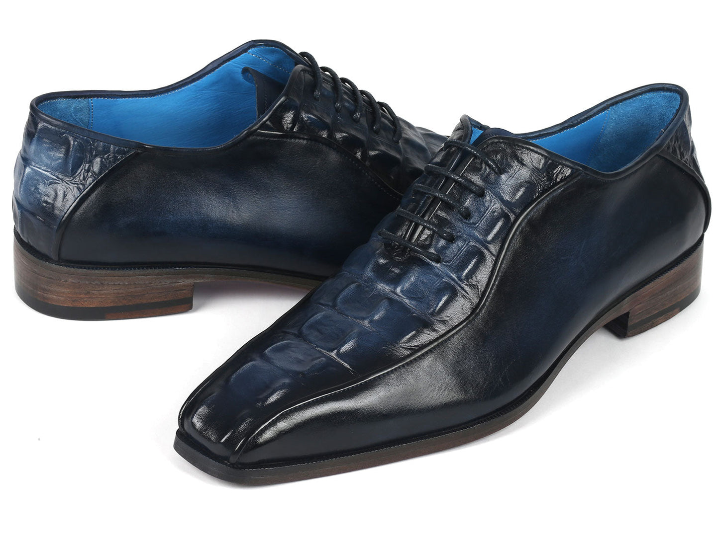 A pair of Paul Parkman Navy Croco Textured Leather Bicycle Toe Oxfords, featuring elegant blue interiors and brown soles, styled with one shoe slightly on top of the other.