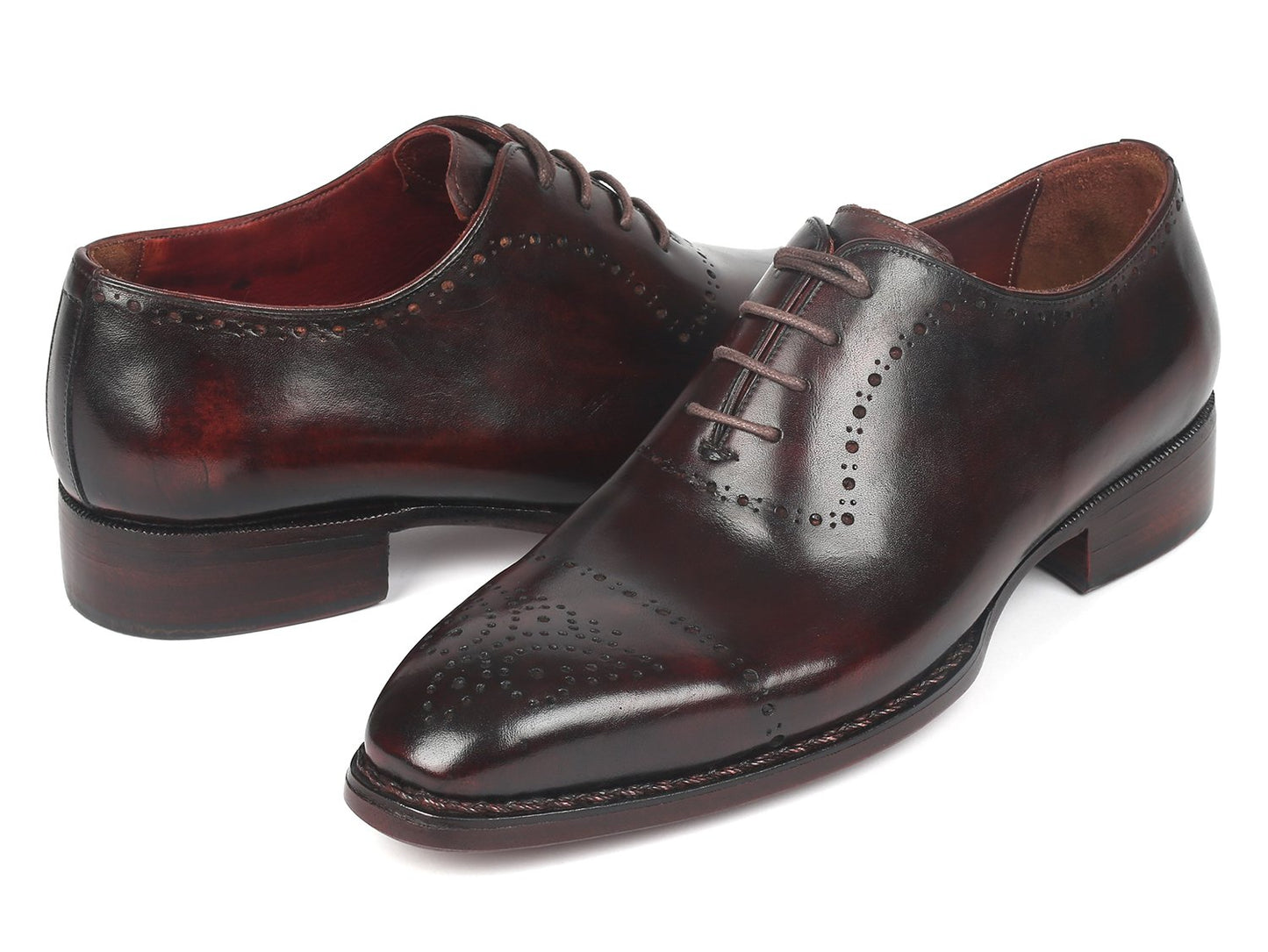 A pair of Paul Parkman Dark Bordeaux Goodyear Welted Oxfords - 56BRD83, featuring polished leather with laces and decorative perforations, is positioned with one shoe slightly raised and overlapped.