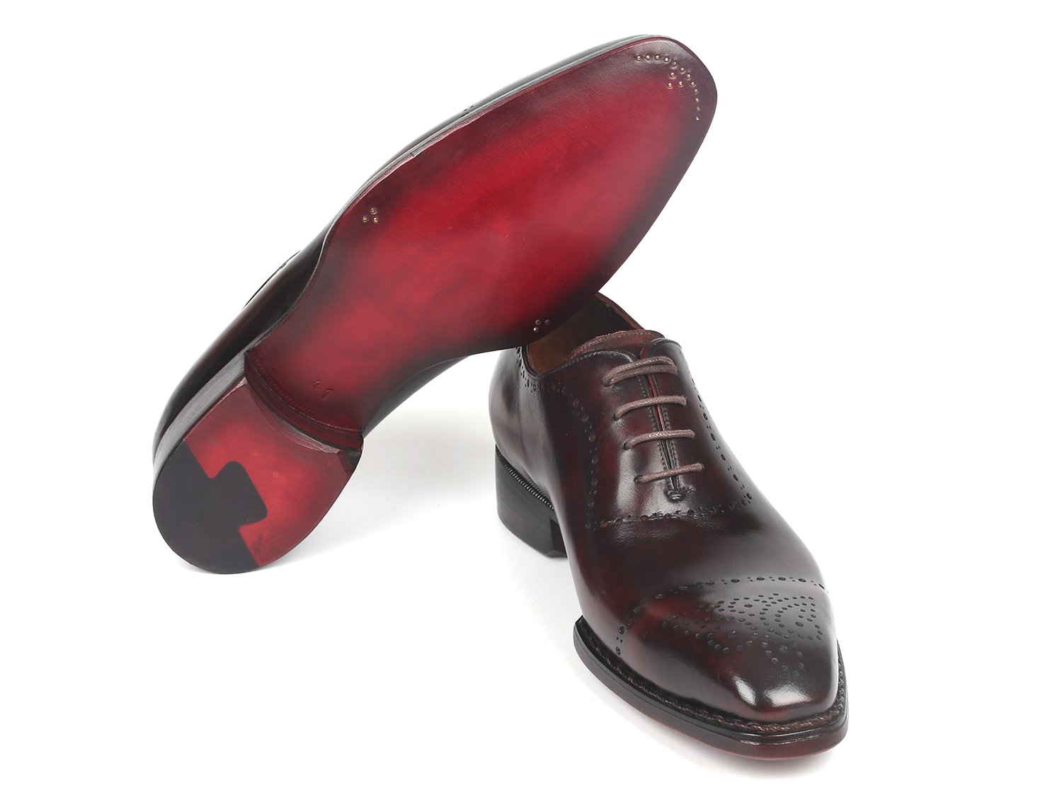 A pair of Paul Parkman Dark Bordeaux Goodyear Welted Oxfords - 56BRD83, featuring polished leather with laces and decorative perforations, is positioned with one shoe slightly raised and overlapped.