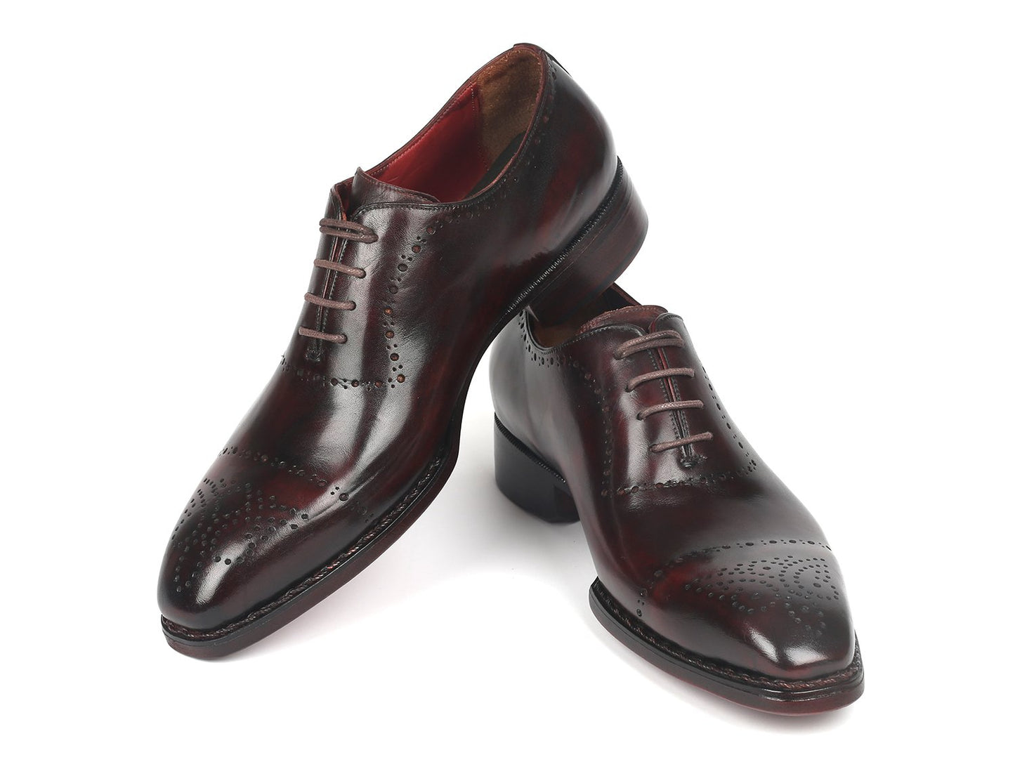 A pair of Paul Parkman Dark Bordeaux Goodyear Welted Oxfords - 56BRD83, featuring polished leather with laces and decorative perforations, is positioned with one shoe slightly raised and overlapped.