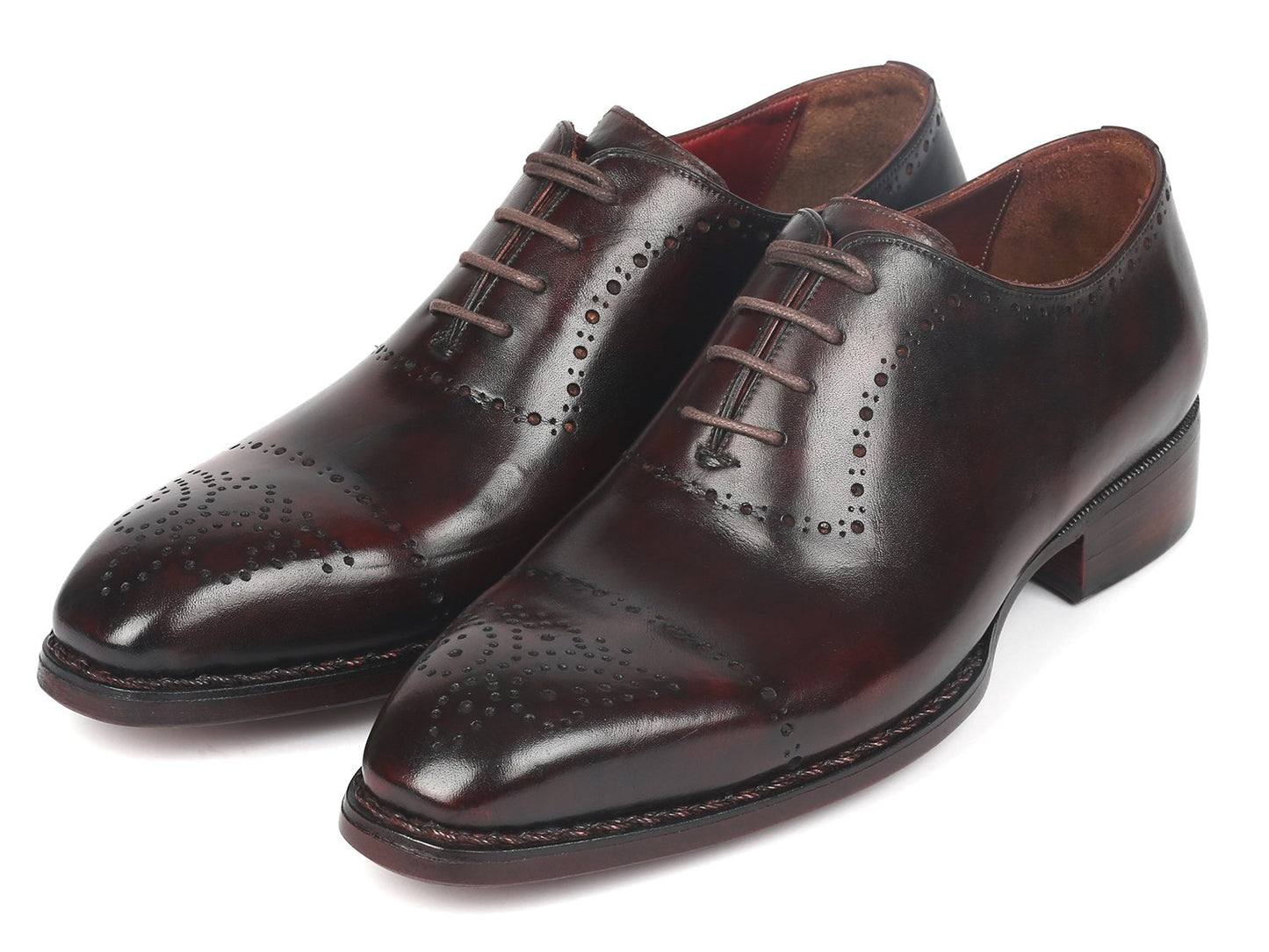 A pair of Paul Parkman Dark Bordeaux Goodyear Welted Oxfords - 56BRD83, featuring polished leather with laces and decorative perforations, is positioned with one shoe slightly raised and overlapped.