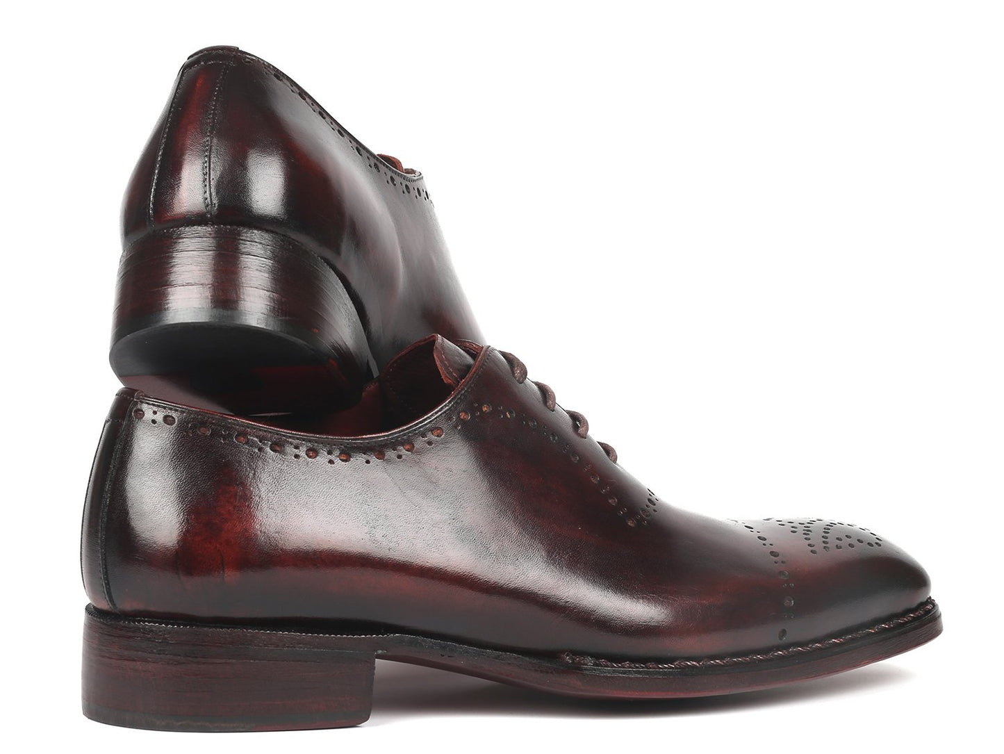 A pair of Paul Parkman Dark Bordeaux Goodyear Welted Oxfords - 56BRD83, featuring polished leather with laces and decorative perforations, is positioned with one shoe slightly raised and overlapped.