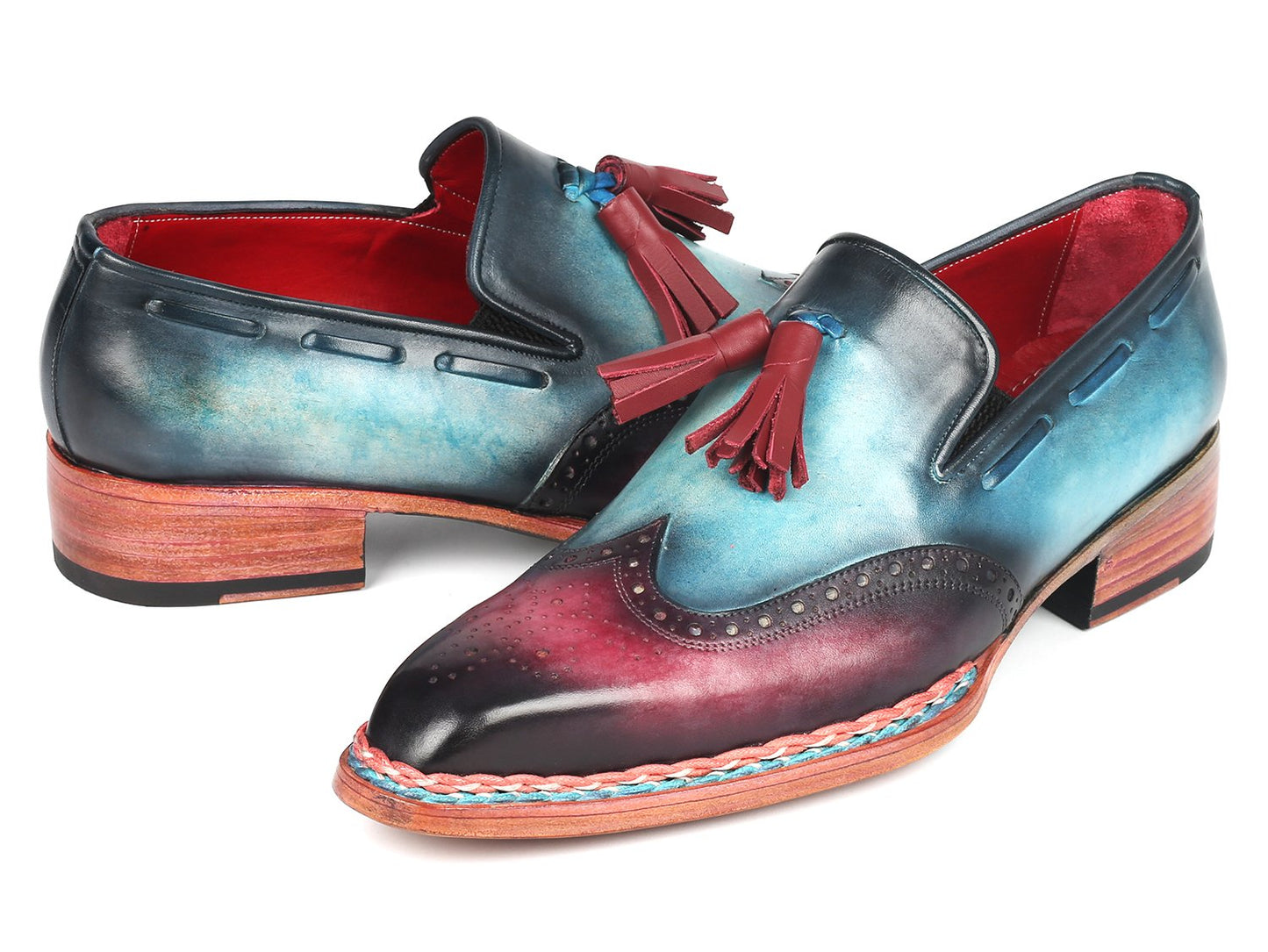 The Paul Parkman Norwegian Welted Tassel Loafers Blue & Purple - 8507-BPR feature hand-painted leather with a stunning gradient from blue to burgundy, adorned with red tassels, intricate brogue detailing, and a vibrant multicolored sole, all showcased against a plain backdrop.