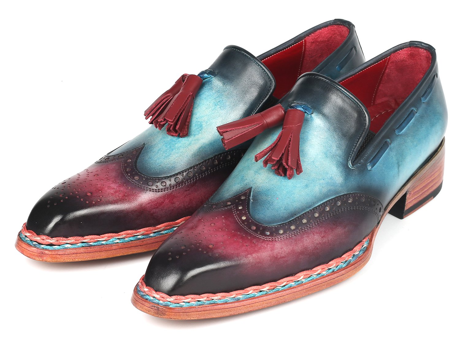 The Paul Parkman Norwegian Welted Tassel Loafers Blue & Purple - 8507-BPR feature hand-painted leather with a stunning gradient from blue to burgundy, adorned with red tassels, intricate brogue detailing, and a vibrant multicolored sole, all showcased against a plain backdrop.