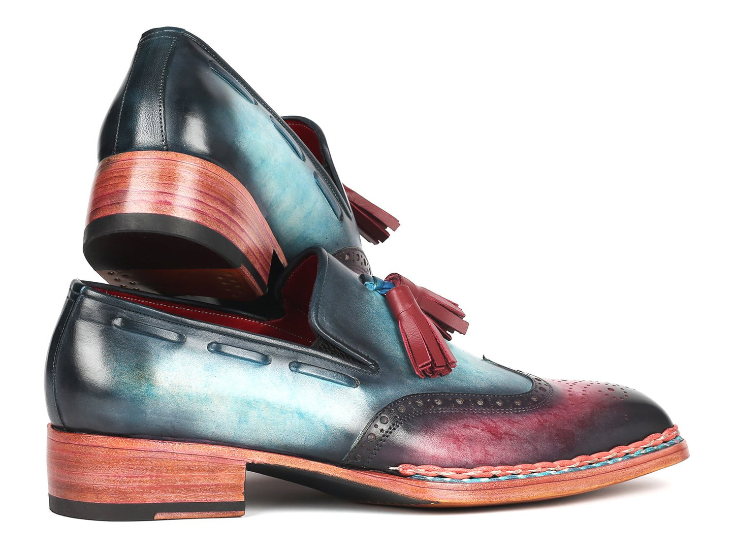 The Paul Parkman Norwegian Welted Tassel Loafers Blue & Purple - 8507-BPR feature hand-painted leather with a stunning gradient from blue to burgundy, adorned with red tassels, intricate brogue detailing, and a vibrant multicolored sole, all showcased against a plain backdrop.