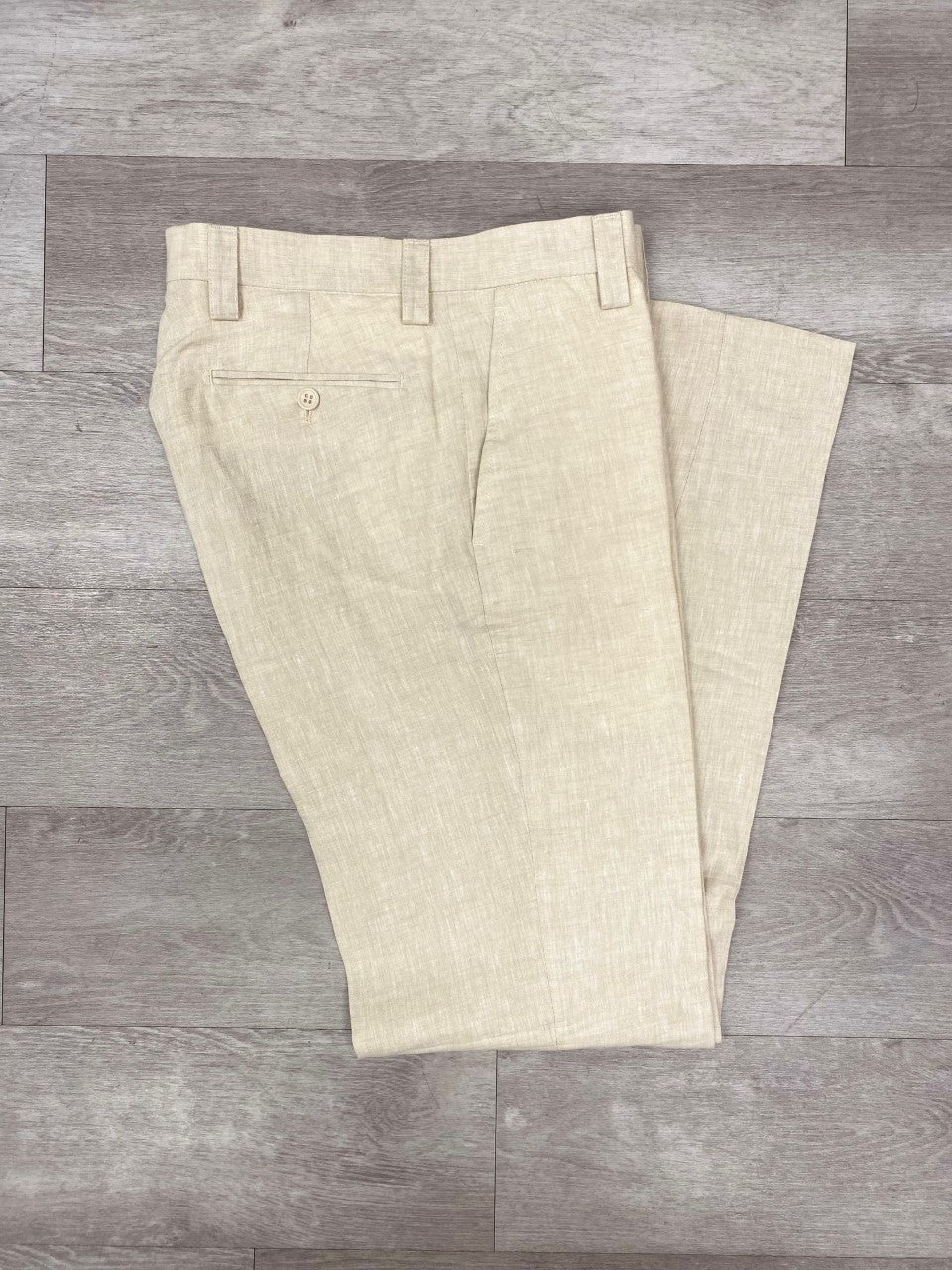 The Inserch Premium Linen Flat Front Pants P3116 in oatmeal rest folded lengthwise on a wooden floor, showcasing a classic design that is ideal for a warm weather outfit.