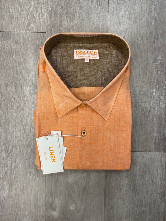 An Inserch Premium Linen Yarn-Dye Solid Long Sleeve Shirt in orange, featuring pearlized buttons, rests on a wooden surface with the tags still attached.