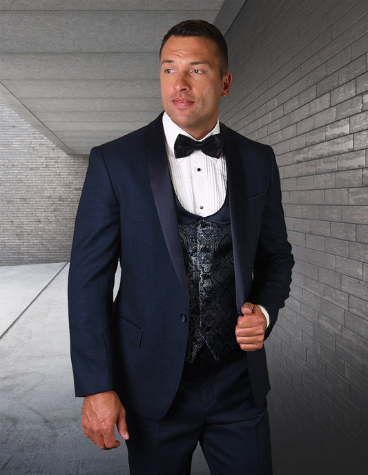 A man in the STATEMENT CLOTHING | PALMERO-INDIGO tuxedo, complete with a bow tie, stands in a hallway with brick walls, showcasing the elegance of Statement Clothing's tailored fit.