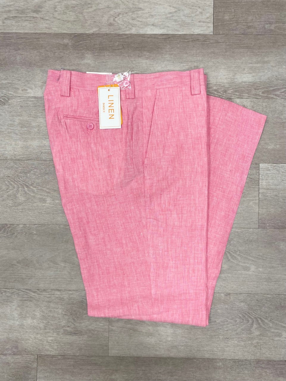 The Inserch Premium Linen Flat Front Pants P3116 in pink, featuring a side pocket and a tag, ideal for warm weather, are showcased on a wooden floor.