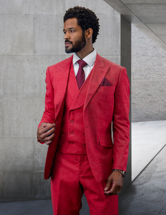 A man wearing the Statement Clothing | RIMA-MAGENTA suit, a striking red double-breasted wool garment with a peak lapel, stands against a gray concrete wall, gazing to the side.