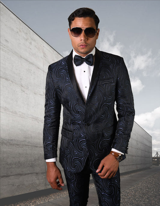 A man wearing the Statement Clothing slim fit suit (RJS-104-NAVY) complete with a coordinating bow tie and sunglasses stands outdoors against a concrete wall.