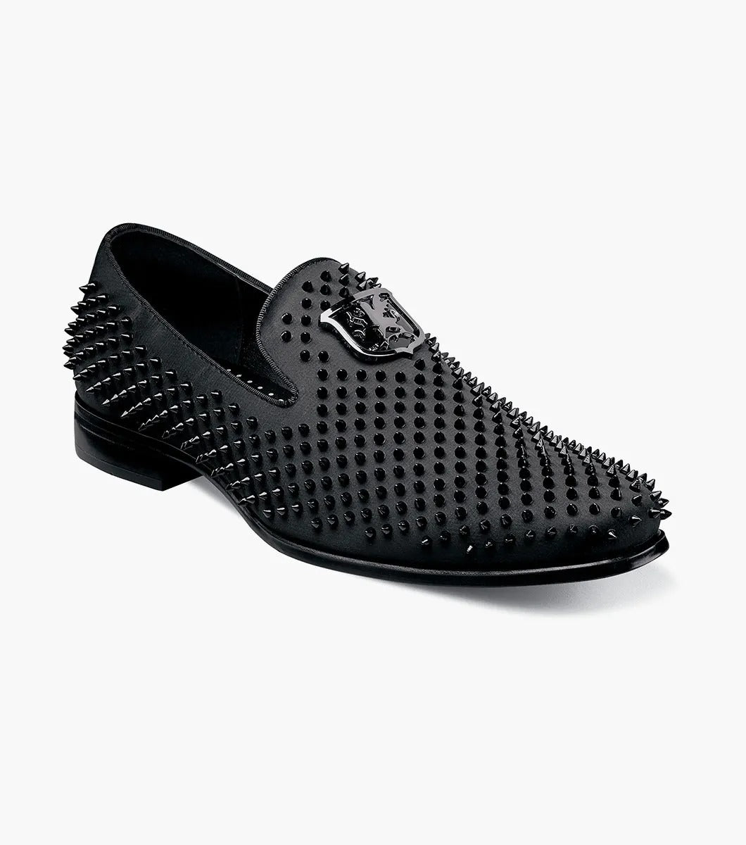 The Stacy Adams SABRE Spiked Slip On (21528-001) boasts a black studded design with a shiny emblem on the upper. Enhanced with Memory Foam, this stylish shoe from STACY ADAMS delivers both flair and comfort, all set against a pristine white background.