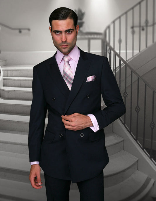 A man in a tailored fit dark suit from Statement Clothing, featuring the STATEMENT CLOTHING | SD-100-NAVY double-breasted jacket paired with flat-front pants, compliments his look with a pink shirt and plaid tie as he stands in front of a staircase.