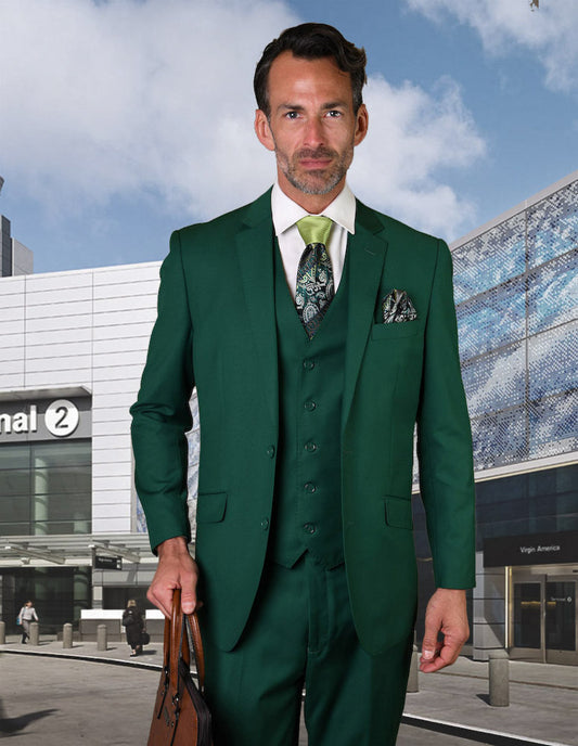 A man dressed in the STATEMENT CLOTHING | STZV-100-FORESTGREEN suit, featuring flat front pants and a tailored fit by Statement Clothing, holds a brown briefcase while standing outside an airport terminal.