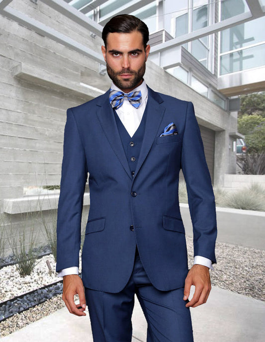 A man in a tailored fit indigo suit and bow tie from Statement Clothing stands outside a modern building, showcasing sleek flat front pants.