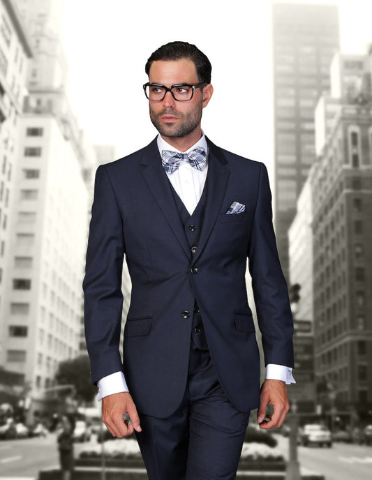 Dressed in the STATEMENT CLOTHING | STZV-100-NAVY by Statement Clothing, a man exudes confidence. His dark suit with a bow tie fits him perfectly with tailored detail and flat front pants as he strides through an urban landscape framed by towering buildings.