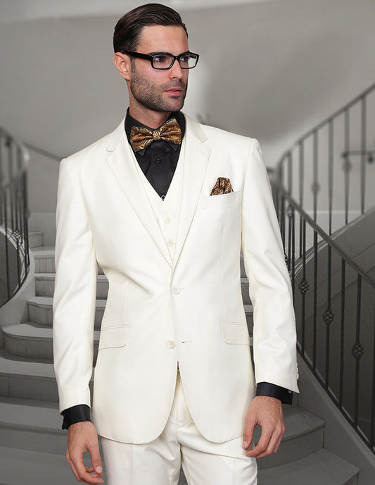 Dressed impeccably in a STATEMENT CLOTHING | STZV-100-OFFWHITE ensemble from Statement Clothing, featuring a tailored fit made with Super 150's fabric, a man showcases confidence in his white suit paired with a black shirt and gold bow tie as he stands before a stairway.