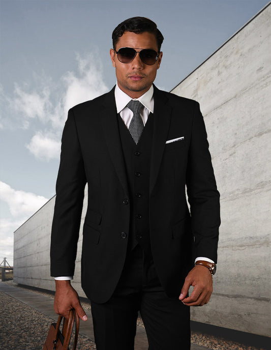 A man wearing the STATEMENT CLOTHING | STZV-101-BLACK tailored fit suit from Statement Clothing and sunglasses holds a brown briefcase, standing outdoors against a concrete wall and cloudy sky. His sleek ensemble, featuring flat front pants, exudes sophistication and modern elegance.