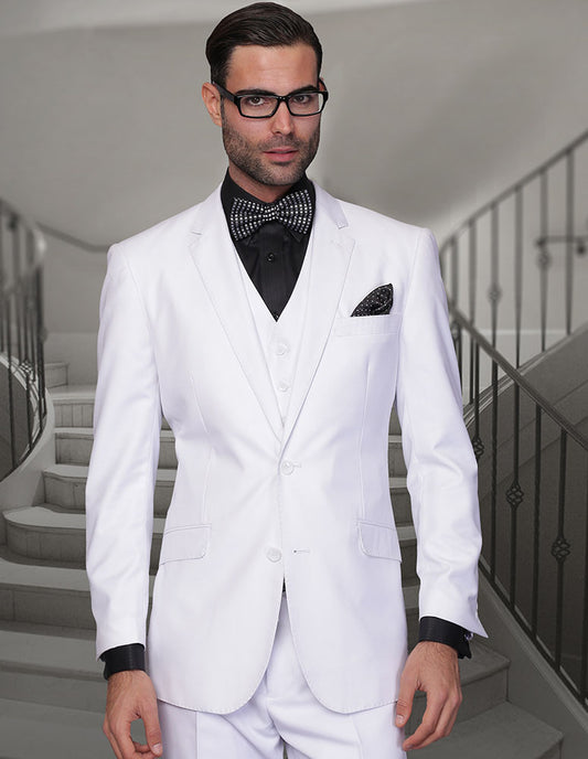 A man wearing the STATEMENT CLOTHING | STZV-102XL-WHITE by Statement Clothing, a modern fit white suit paired with a black shirt and polka dot bow tie, stands confidently in front of a staircase.