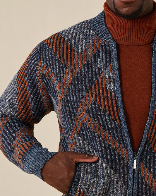 A person wearing the Inserch Sherpa-lined Baseball Collar Full Zip Sweater SW606-11 in Navy, styled with a cozy regular fit over a rust-colored turtleneck. The cotton blend sweater showcases diagonal lines and geometric shapes for added flair as the individual’s hand rests casually in their pocket.