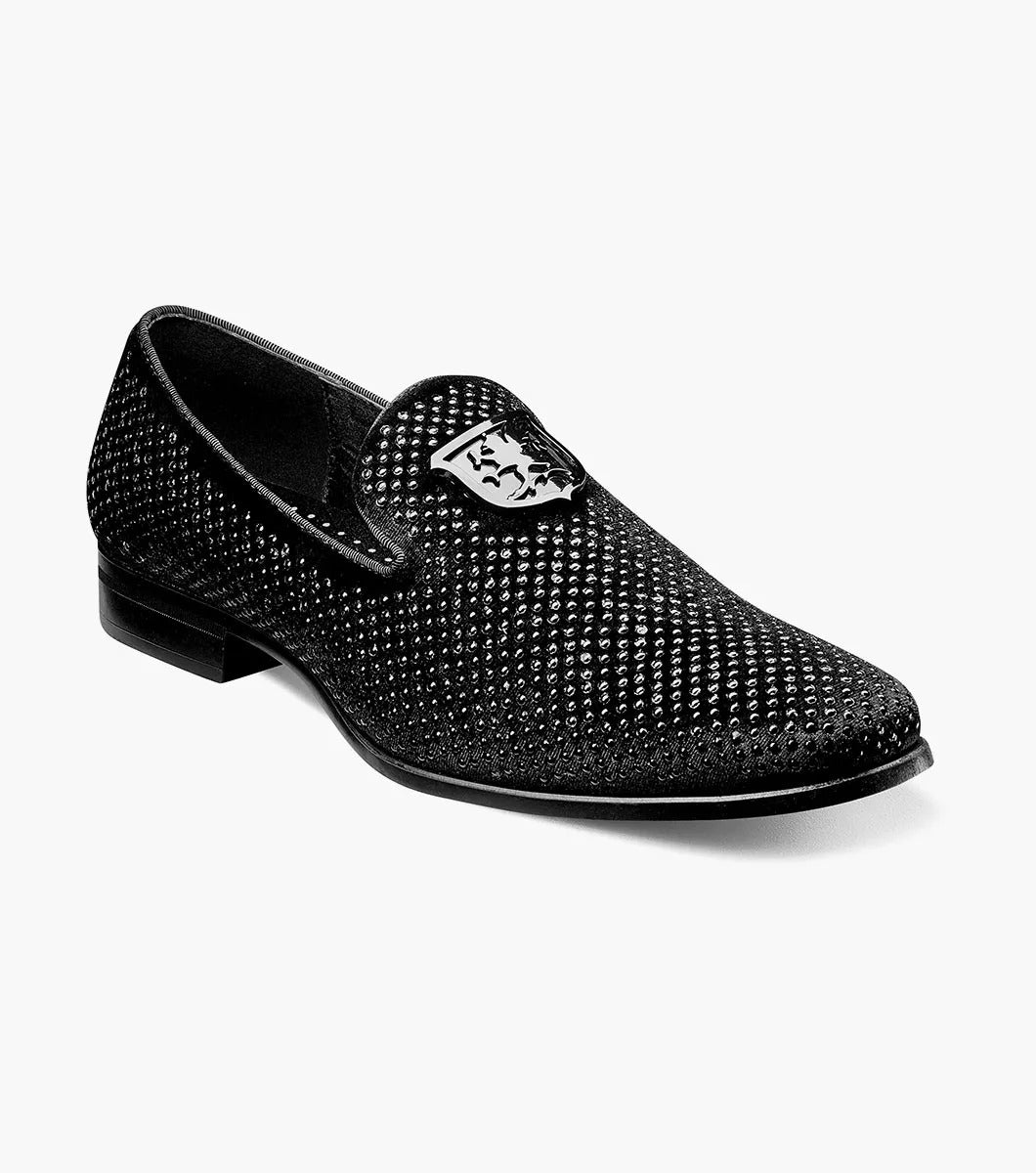 The Stacy Adams - SWAGGER Studded Slip On in black (style 25228-001) features a striking silver emblem, accompanied by a textured design and low heel. These shoes offer a sophisticated touch with the added comfort of memory foam, making them ideal for any occasion.