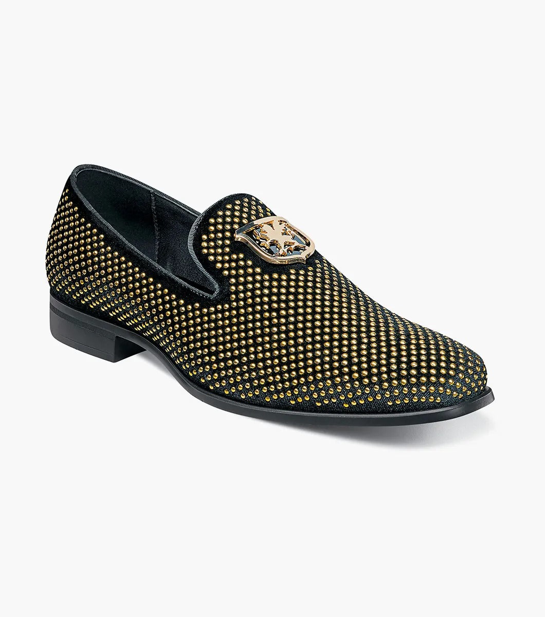 The Stacy Adams - SWAGGER Studded Slip On - Black and Gold - 25228-715 is a black loafer adorned with gold studs and a decorative emblem on top, featuring a comfortable memory foam insole.