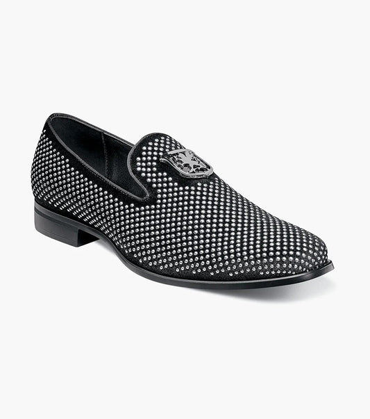 The STACY ADAMS SWAGGER Studded Slip On in black and silver, model 25228-042, is a loafer featuring striking silver studs and the Stacy Adams crest on the upper, exuding a sense of understated elegance.
