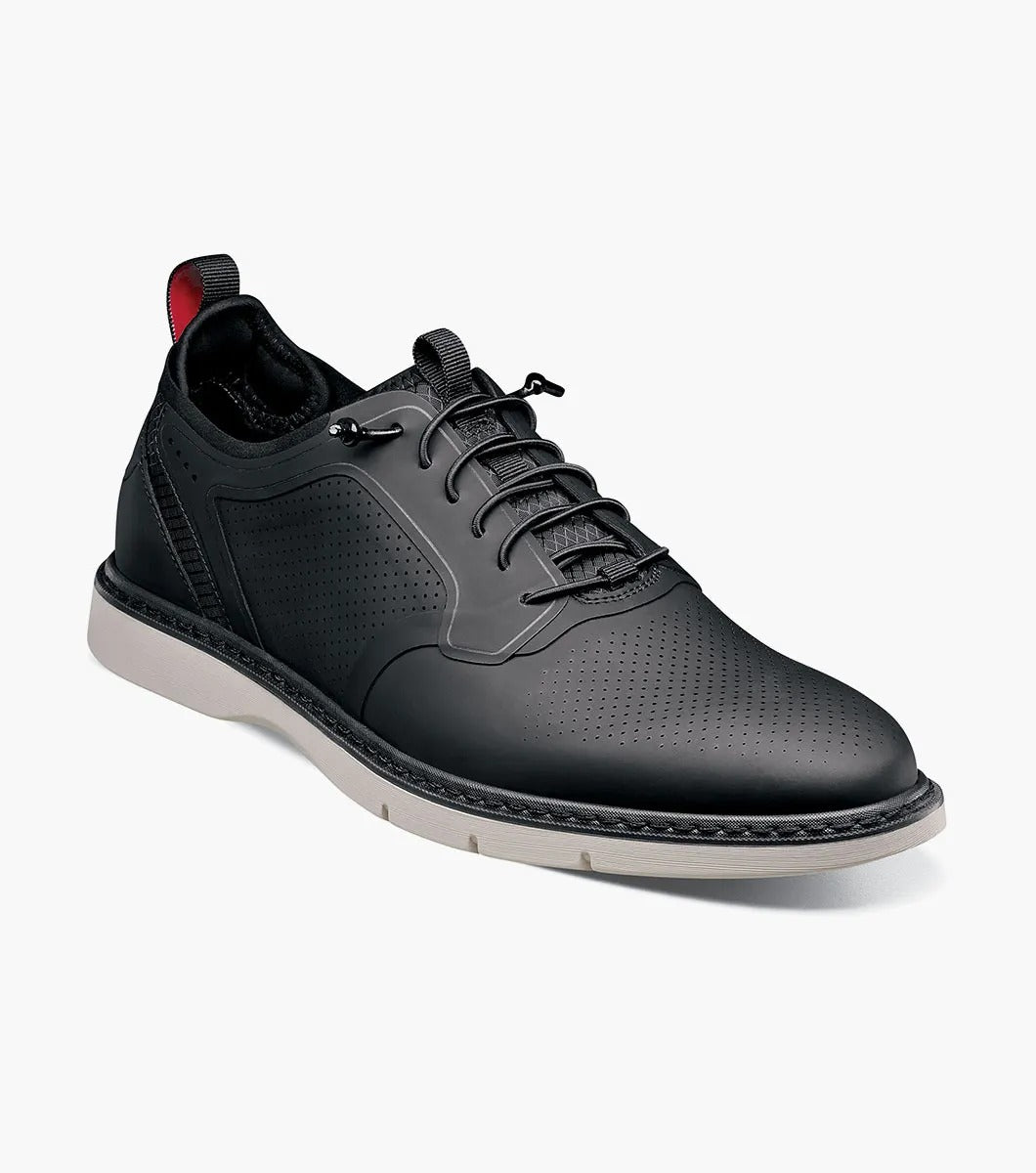 The Stacy Adams SYNCHRO Plain Toe Elastic Lace Up shoe in black (style 25518-001) is a casual dress shoe featuring an elastic lace-up design with a perforated pattern and white sole, complemented by the comfortable RedZone footbed. It is showcased from the side against a simple backdrop.