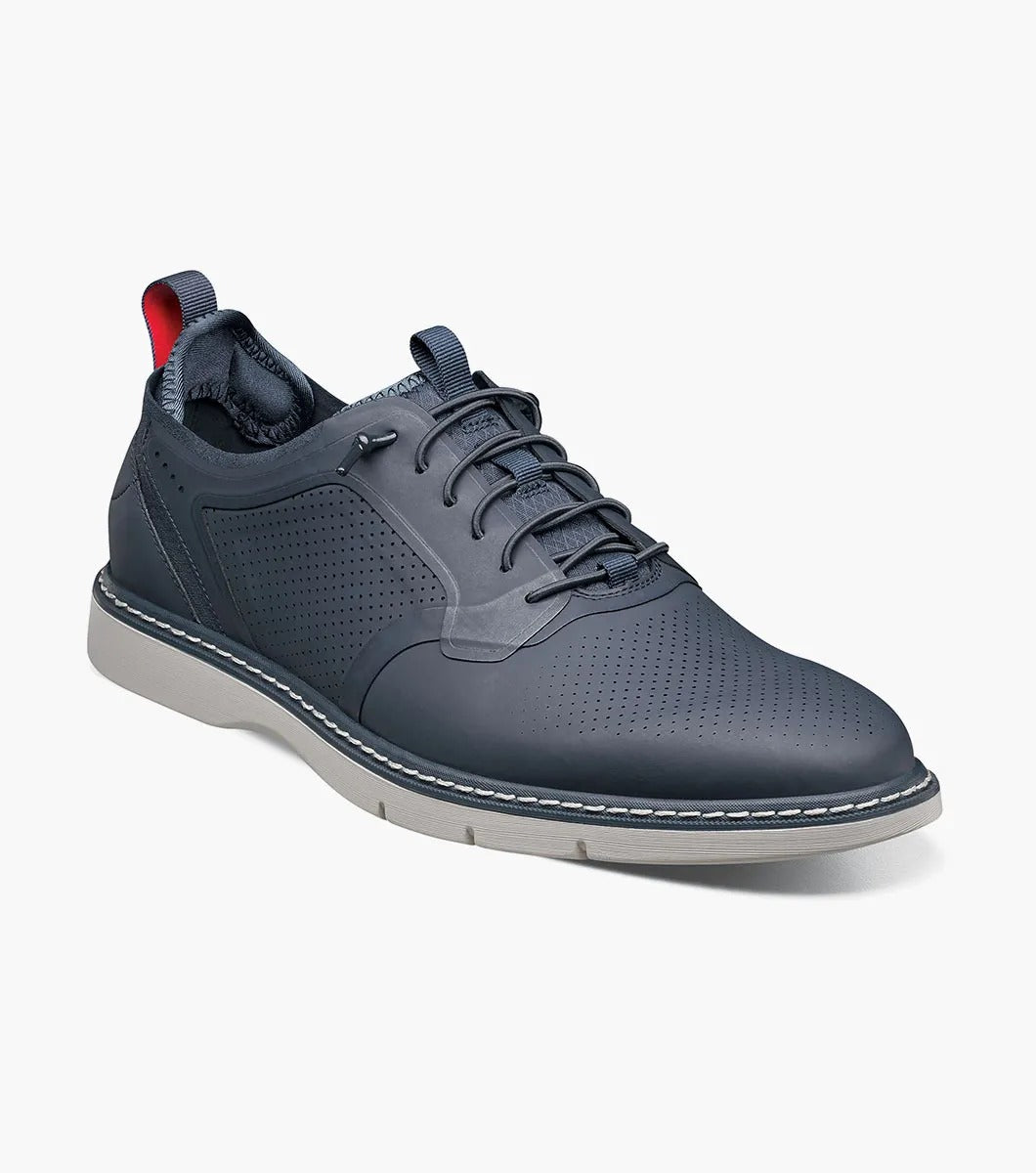 The Stacy Adams SYNCHRO Plain Toe Elastic Lace Up shoe in navy boasts a perforated pattern and a red pull tab, complemented by a light gray sole. It is designed with the RedZone removable footbed to provide anatomical arch support.