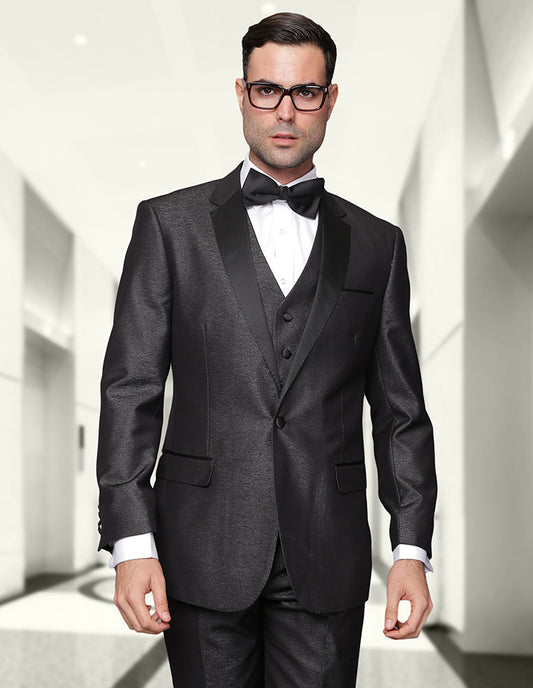 A man dressed in Statement Clothing's TURIN-2-BLACK, expertly tailored from fine Italian wool, paired with a waistcoat and bow tie, stands in a brightly lit corridor with a neutral expression. Sporting glasses and dark hair, his ensemble boasts a modern fit.