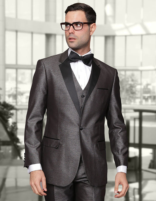 A man dressed in the STATEMENT CLOTHING | TURIN-2-GRAY, a tuxedo made from luxurious Italian wool with a modern fit, sports a black bow tie and glasses as he stands indoors facing slightly to the side.