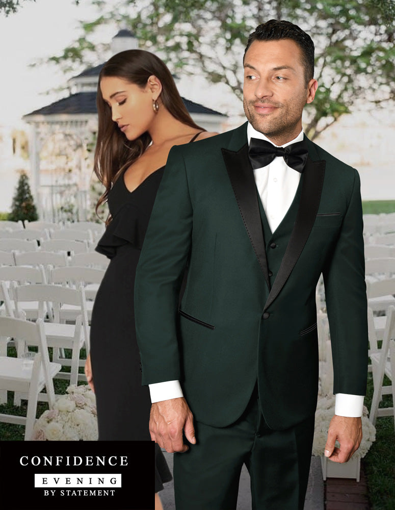 A man in a Statement Clothing TUX-PK-HUNTER tuxedo with tailored fit and a woman in a black dress stand elegantly in front of white chairs set up outdoors, while a gazebo provides the perfect backdrop.