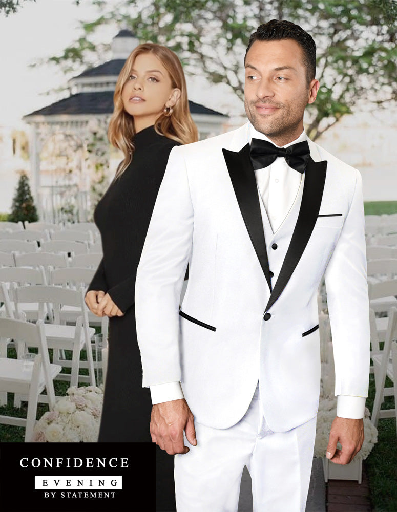 A man in a tailored fit tuxedo from Statement Clothing's TUX-PK-WHITE collection stands confidently with a woman in a black dress behind him. They are outdoors, poised in front of a seating area arranged for an elegant event.