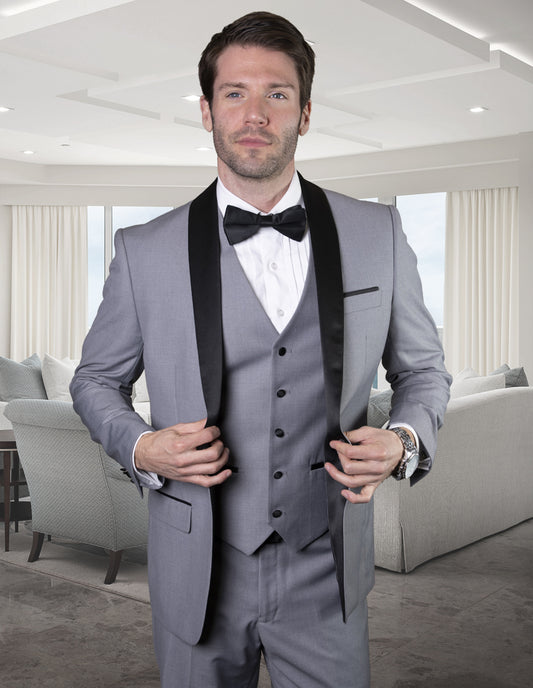 A man in a tailored-fit STATEMENT CLOTHING | TUX-SH-GREY from Statement Clothing, complete with a black bow tie, stands in a modern living room.