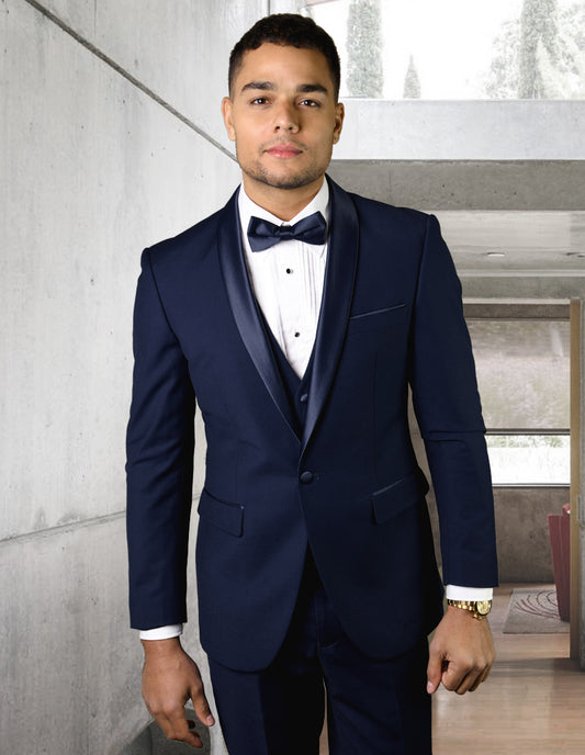 A gentleman wearing the Statement Clothing TUX-SH-NAVY stands indoors, highlighting its tailored fit and elegant shawl lapel against the backdrop of a concrete wall and large windows.