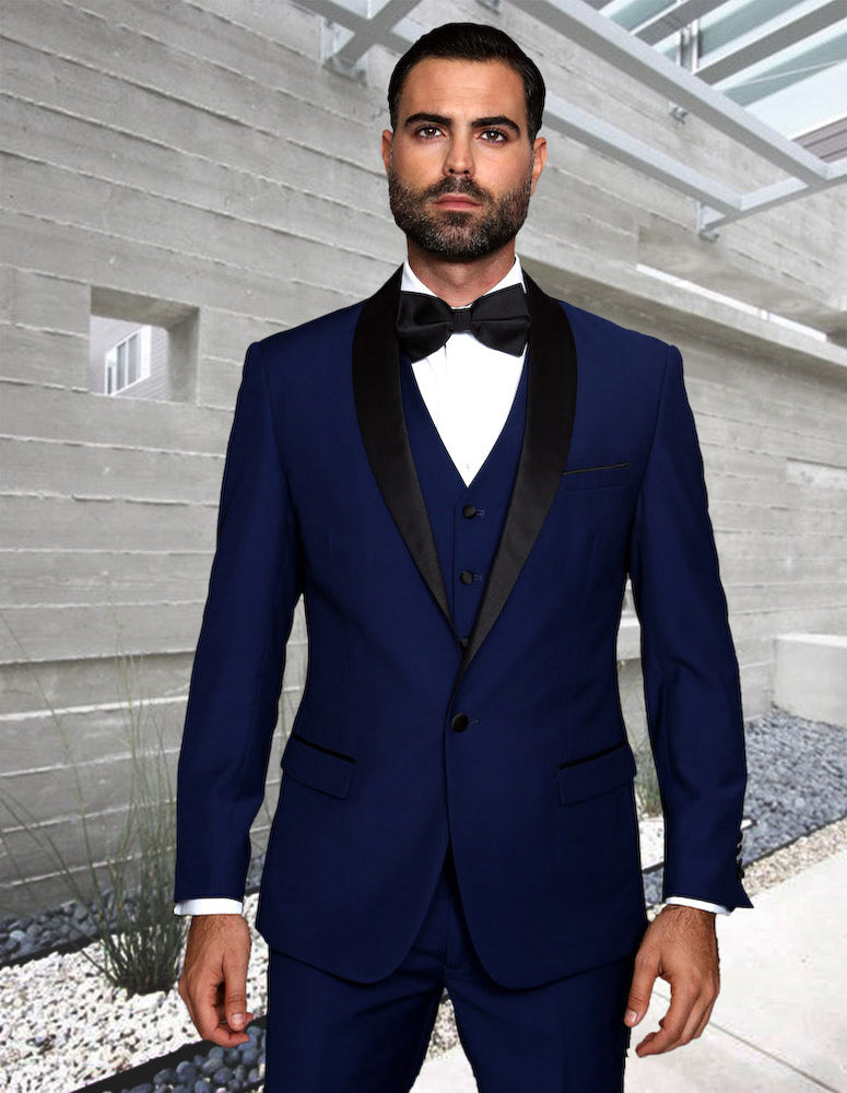 A man wearing the STATEMENT CLOTHING | TUX-SH-SAPPHIRE by Statement Clothing, paired with a black bow tie, stands in front of a modern concrete building.