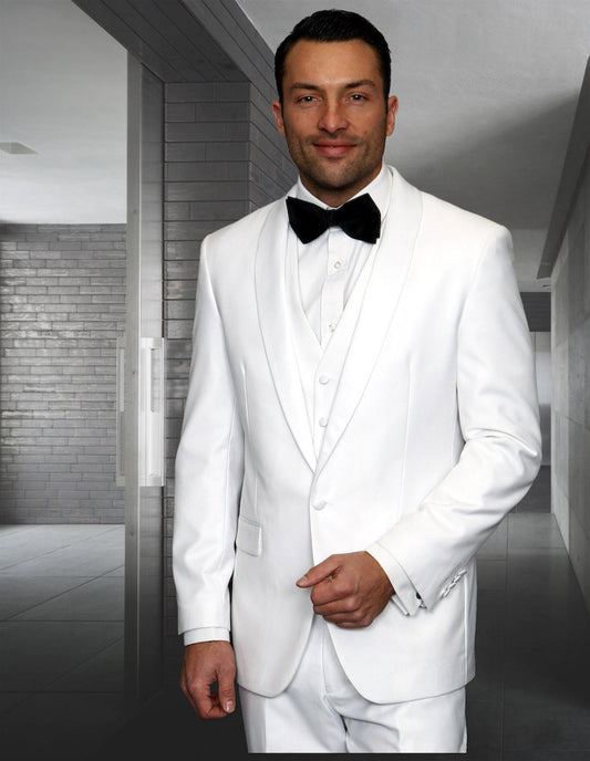 A man wearing the STATEMENT CLOTHING | TUX-SH-WHITE by Statement Clothing, featuring a tailored fit with a black bow tie and classic shawl lapel, stands in a modern hallway with gray brick and tile walls, exuding elegance.