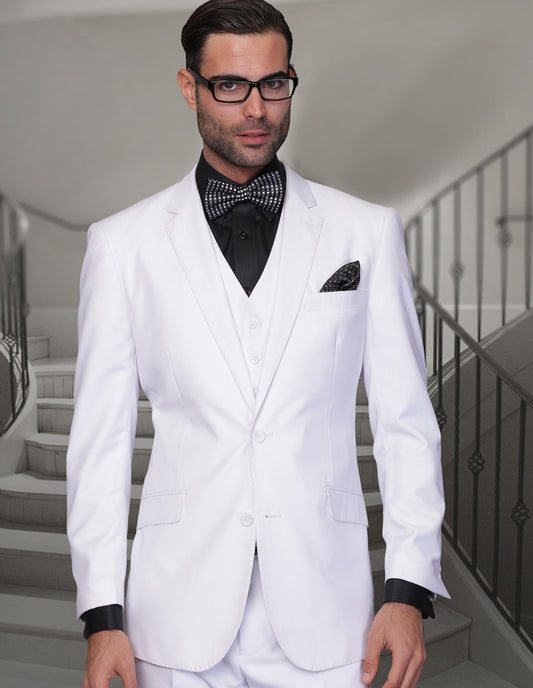 A man in the STATEMENT CLOTHING | TZ-100-WHITE by Statement Clothing, crafted from Super 150's fabric, paired with a black shirt and bow tie, stands confidently in front of a staircase. The ensemble features regular fit pleated pants, enhancing his polished and elegant appearance.