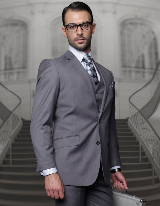 A man in a charcoal suit crafted from luxurious Super 150's fabric by Statement Clothing, featuring pleated pants and a regular fit, holds a briefcase as he stands before an ornate staircase.